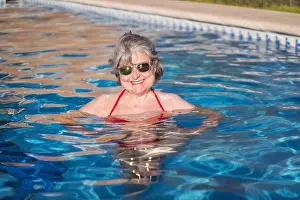 Pleasant Prints: Cheerful elderly female with gray hair swimming in pool and brightly smiling at camera with sunglasses