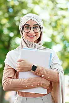 Satisfied Prints: Cheerful glad cute young arab muslim female student in hijab and glasses holds books
