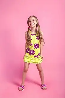 Cheerful little child girl in summer dress posing on a colored pink background