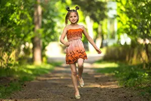 Cheerful little girl running along a path in a park