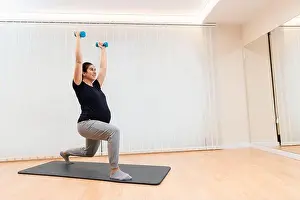 Practicing Prints: A cheerful pregnant doing lunges with light dumbells exercises on a mat at health center