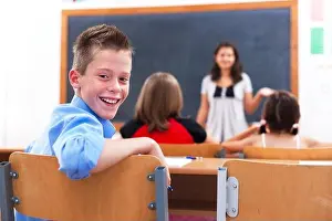 Turning Prints: Cheerful school boy looking back in class room while the teacher explains