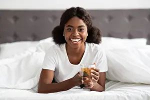 Satisfied Prints: Cheerful young black woman enjoying herbal tea in bed