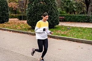 Satisfied Prints: Cheerful young female in activewear and sneakers running on path while training in green park