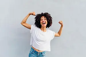 Curly Hair Prints: Cheerful young woman flexing muscles in front of white wall