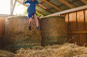 Family Vacation Prints: A child jumps from a bale of hay in a barn, face not visible, depersonalization photo