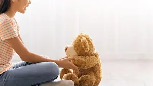 Teddy Prints: Child Sits on Floor With Teddy Bear Looking at Each Other in a Bright Indoor Space