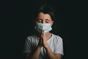 Urgency Prints: child wearing medical mask for coronavirus with hands clasped together praying over black background