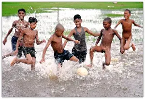 Children playing football at a swampy field on a hot summer day in Bakulia, Chittagong, Bangladesh. May 24, 2007