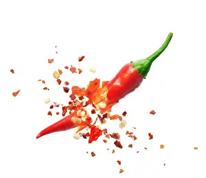 Explode Prints: Chili flakes bursting out from red chili pepper over white background