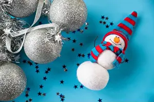 Christmas Decoration Prints: Christmas and New Year needle felted snowman in red blue knitted hat on blue background with silver christmas ornaments