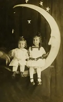 Curtains Prints: Circa 1910 photograph of a young boy and girl sitting on a paper moon. Studio photograph