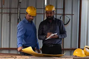 Coworker Prints: Civil engineer holding a blueprint while colleague is taking notes into notepad