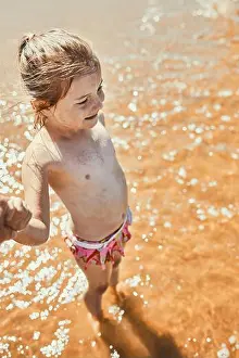 Sand Beach Prints: Close up of happy little girl standing in the sea looking away holding parent's hand