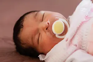 Asleep Prints: Close up portrait of a cute two weeks old newborn baby girl wearing soft pink knit clothes