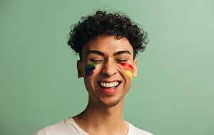 Generation Z Prints: Close-up of a cheerful young man with pride flag painted on face