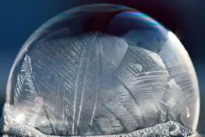 Close-up macro of a frozen soap bubble with abstract pattern in winter sunlight, isolated on blue