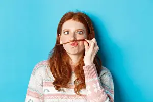 Redhead Prints: Close-up of silly and funny redhead girl making moustache with hair strand and puckered lips