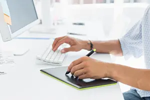 Computer Monitor Prints: Close-up side view of an artist drawing something on graphic tablet with pen