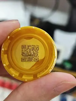 Genuine Prints: Close-up of a yellow plastic bottle cap with embedded QR code