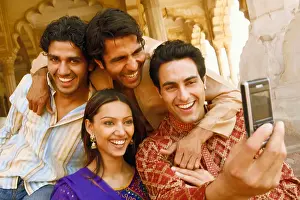 25 30 Years Prints: Close-up of three young men and a young woman looking at a mobile phone and smiling