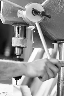 Woodwork Prints: Close up view of a carpenter's hands operating a bench drill press on a piece of wood in a workshop