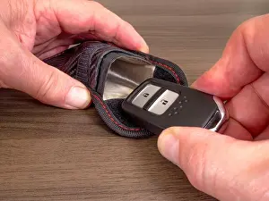 Pouch Prints: Closeup of a man's hands sliding a keyless fob in our out of a radio signal-blocking / Faraday pouch
