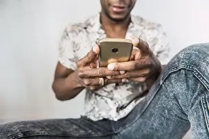 Texting Prints: Closeup of shiny modern mobile phone in hands of black man sitting against white wall