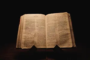 A closeup shot of a historic old Bible open on the Jonah pages on display in a dark room