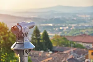 Closeup shot of touristic telescope against italian vilage at sunset. Warm sunset light