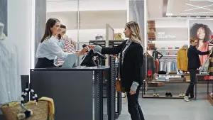 Clothing Store Checkout Cashier Counter: Beautiful Young Woman Buys Blouse from Friendly Retail Sales assistant