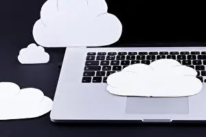 Connected Prints: Cloud computing concept with cutout clouds above a laptop computer keyboard on a black background