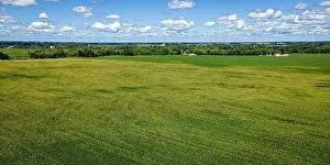 A cloudy blue sky extends to the horizon with a massive farm field below surrounded by a rural area in Wisconsin