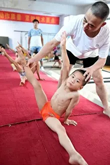 A coach adjusts the posture of a young Chinese boy on the ground to practice gymnastics at a gymnastics training center in Bozhou city, east Chinas An