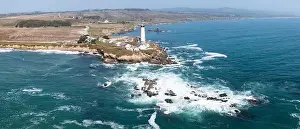 Cold Pacific Ocean waves crash against the rugged and scenic northern California coastline where a lighthouse stands just north of Santa Cruz