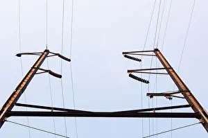 Upward Prints: Color horizontal image looking up at some energy poles and electric wires in front of a blue sky