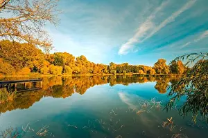 Colorful foliage tree reflections in calm pond water on a beautiful autumn day. Bright autumn trees with tranquil sky, autumn foliage over lake