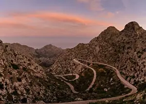 Snake Road Prints: Colourful sunrise in the Tramuntana mountains of Mallorca with a view of the landmark snake road leading down to Sa
