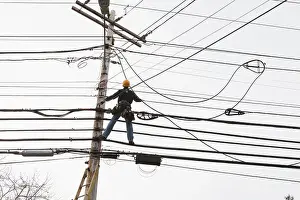 Repairing Prints: Communications worker on a power pole installing new cable to existing bundles
