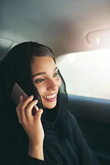 Middle Aged Prints: On call in commute. a young muslim businesswoman using hers phone while traveling in a car