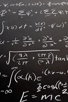 Complicated math wave equation formula ending with E=MC2 with chalk on a blackboard