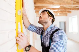 Measuring Prints: Concentraated builder in uniform holding a level against the wall indoors