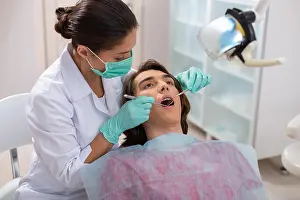 Dentistry Prints: Concentrated woman dentist leaning over her male patient