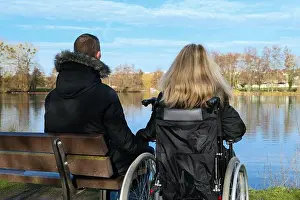 Paralysis Prints: Concept of a disabled person. A blonde woman in a wheelchair who gives her hand to a man sitting on a bench next to her