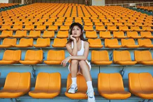 Slender Prints: Confident Asian athletic Woman in sportswear sitting on stadium seat while resting after workout and looking at camera