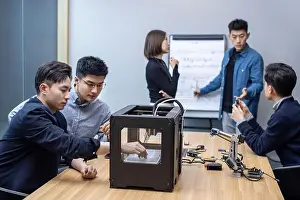 Three Quarter Prints: Confident Chinese designers collaborating around a 3D printer in a modern office
