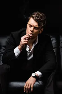 Tobacco Prints: confident man smoking cigarette and sitting on couch isolated on black