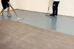 Cleaner Prints: A construction workers applying grey epoxy resin in an industrial hall