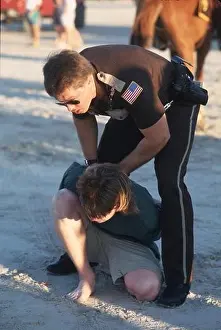 Corpus Christi, Texas USA: Police officer patrolling beach during spring break arrests a young man. ©Bob Daemmrich