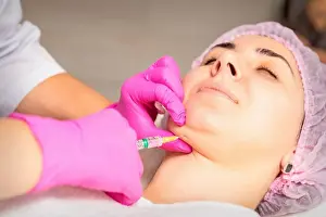 Cheek Prints: The cosmetologist makes lipolytic injection on the chin of a young woman against the double chin in a beauty salon